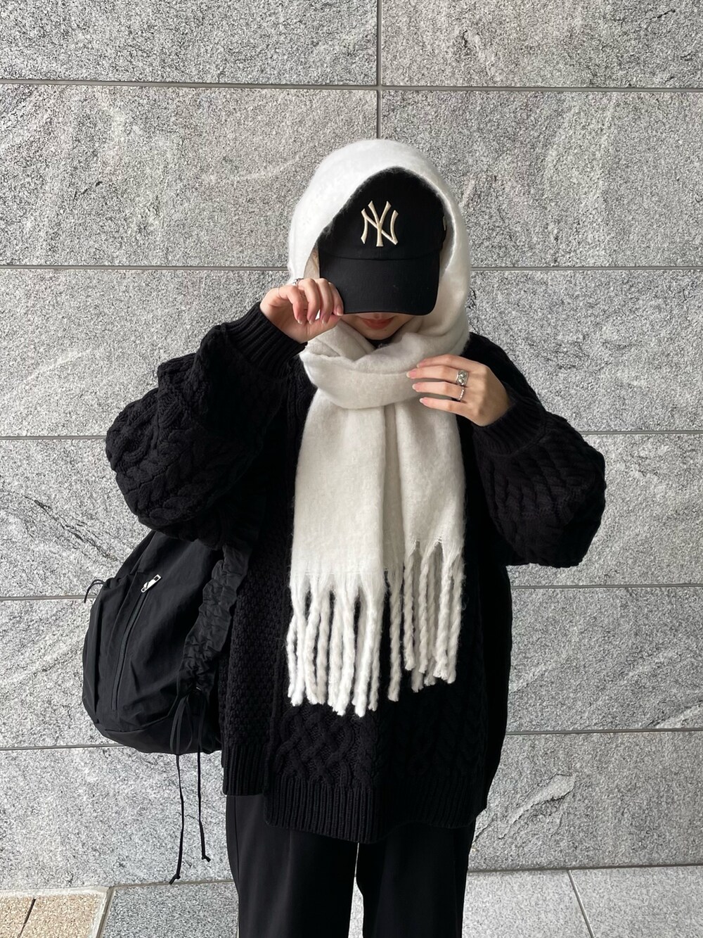 ブラック系のショルダーバッグ、ブラック系のニット/セーター、ホワイト系のマフラーを着用したレディースの冬コーディネートの3枚目の写真