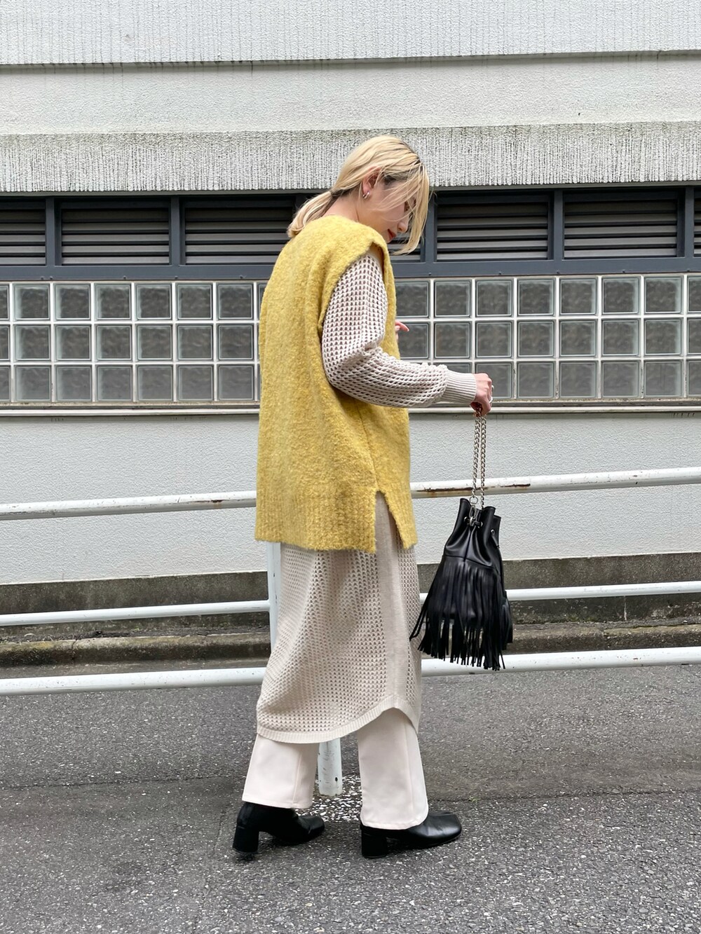 イエロー系のベスト、ブラック系のショルダーバッグ、ホワイト系のワンピースを着用したレディースの秋コーディネートの2枚目の写真