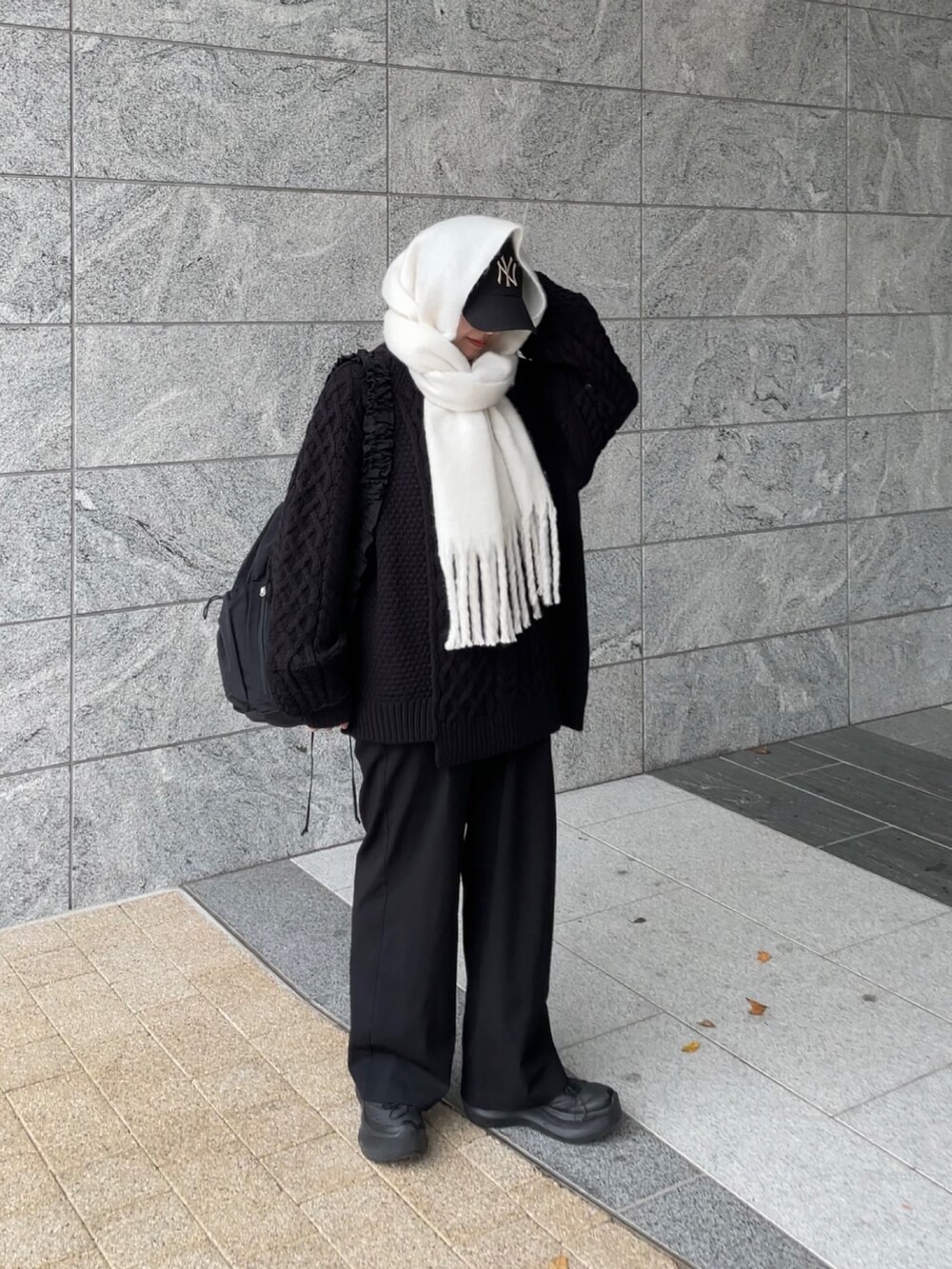 ブラック系のショルダーバッグ、ブラック系のニット/セーター、ホワイト系のマフラーを着用したレディースの冬コーディネートの2枚目の写真