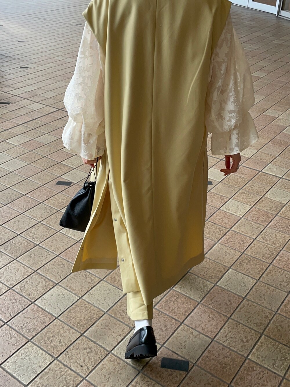 イエロー系のベスト、ホワイト系のシャツ/ブラウス、イエロー系のスラックスを着用したレディースの春コーディネートの2枚目の写真