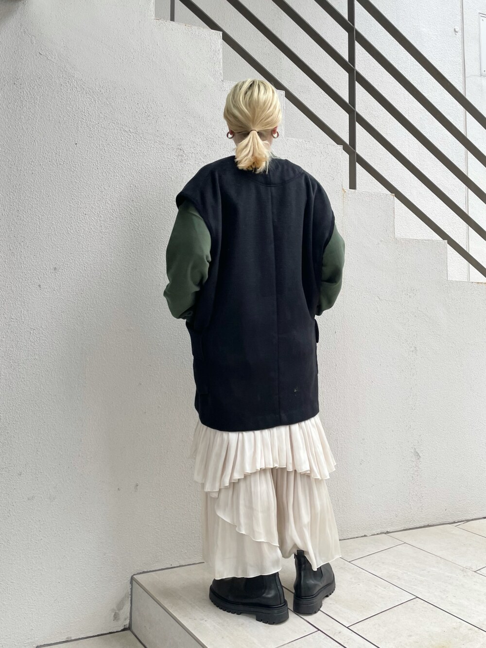 ブラック系のベスト、グリーン系のTシャツ/カットソー、ホワイト系のスカートを着用したレディースの秋コーディネートの2枚目の写真