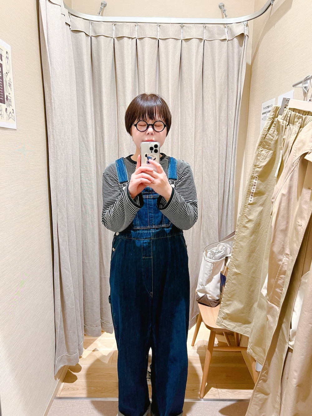 ベージュ系のステンカラーコート、ブルー系のサロペット/オーバーオール、ブラック系のTシャツ/カットソーを着用したレディースの冬コーディネートの2枚目の写真