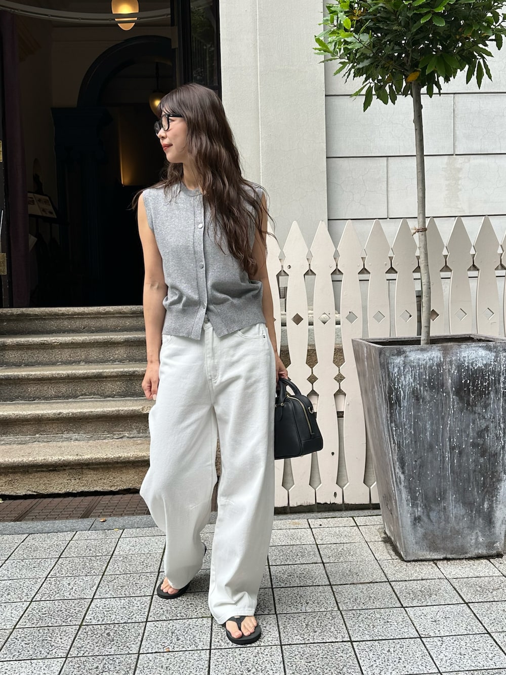 シルバー系のベスト、ホワイト系のデニムパンツ、ブラック系のバッグを着用したレディースの夏コーディネートの2枚目の写真