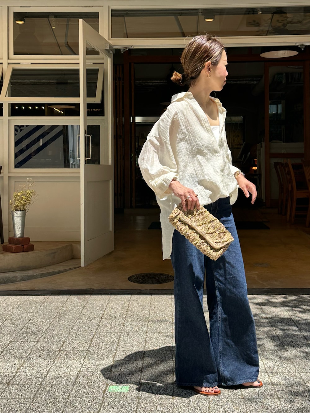 ブルー系のデニムパンツ、ホワイト系のシャツ/ブラウス、ベージュ系のクラッチバッグを着用したレディースの春コーディネートの2枚目の写真