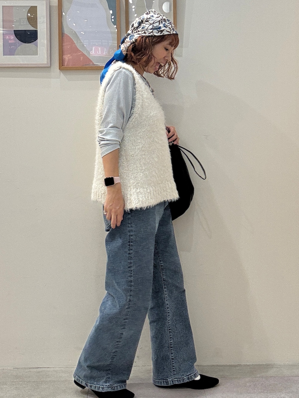 ホワイト系のベスト、ブルー系のデニムパンツ、ブラック系のショルダーバッグを着用したレディースの秋コーディネートの2枚目の写真