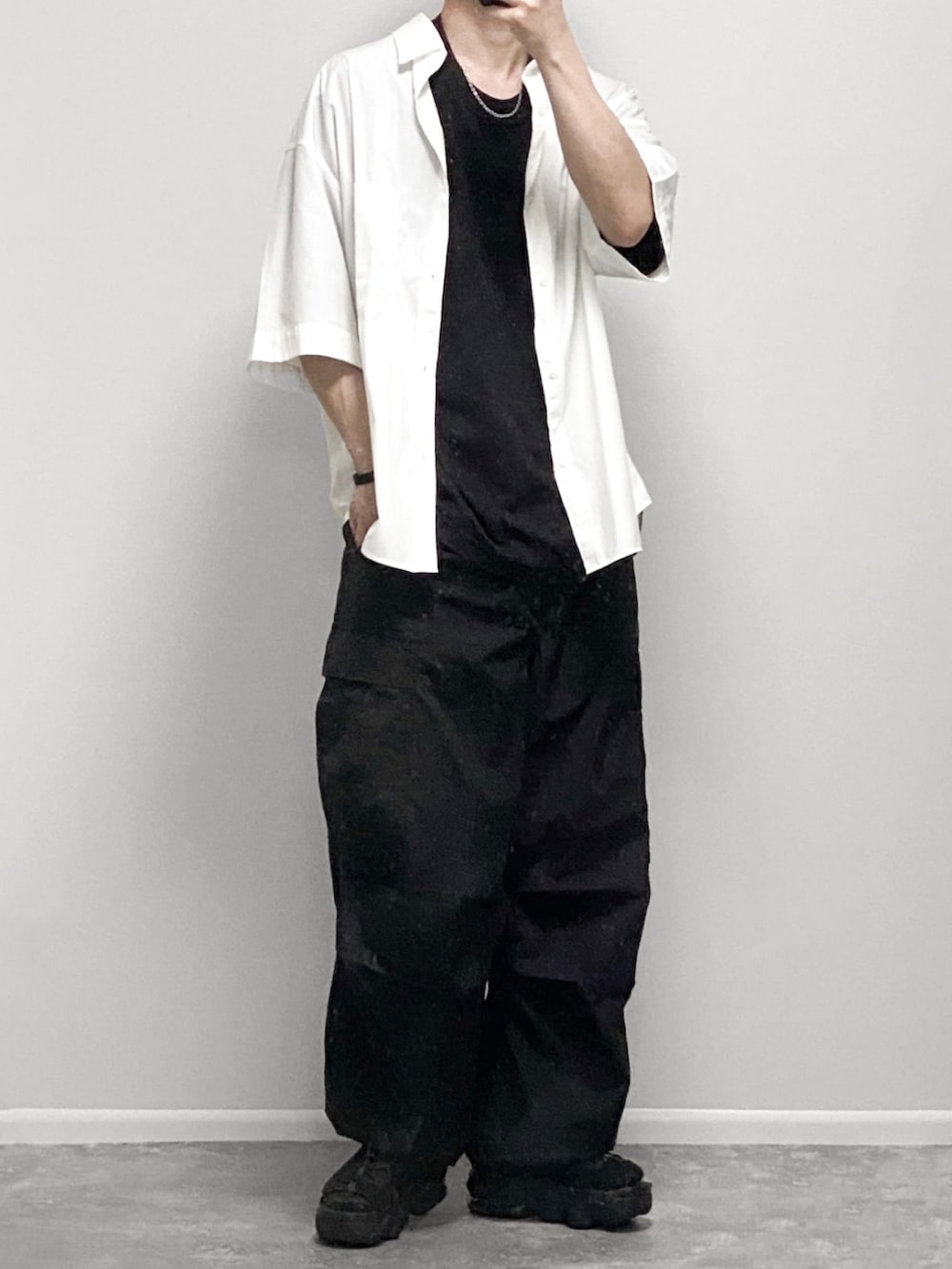 ブラック系のポロシャツ、ブラック系のカーゴパンツ、ホワイト系のバッグを着用したメンズの夏コーディネートの2枚目の写真