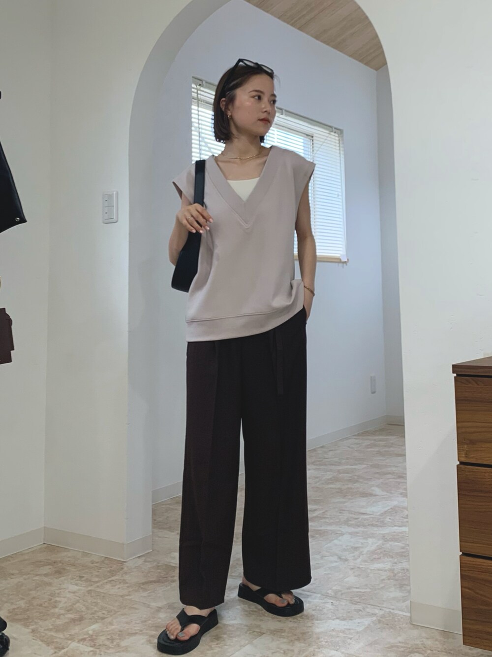 グレー系のベスト、ブラウン系のスラックス、ブラック系のショルダーバッグを着用したレディースの春コーディネートの2枚目の写真