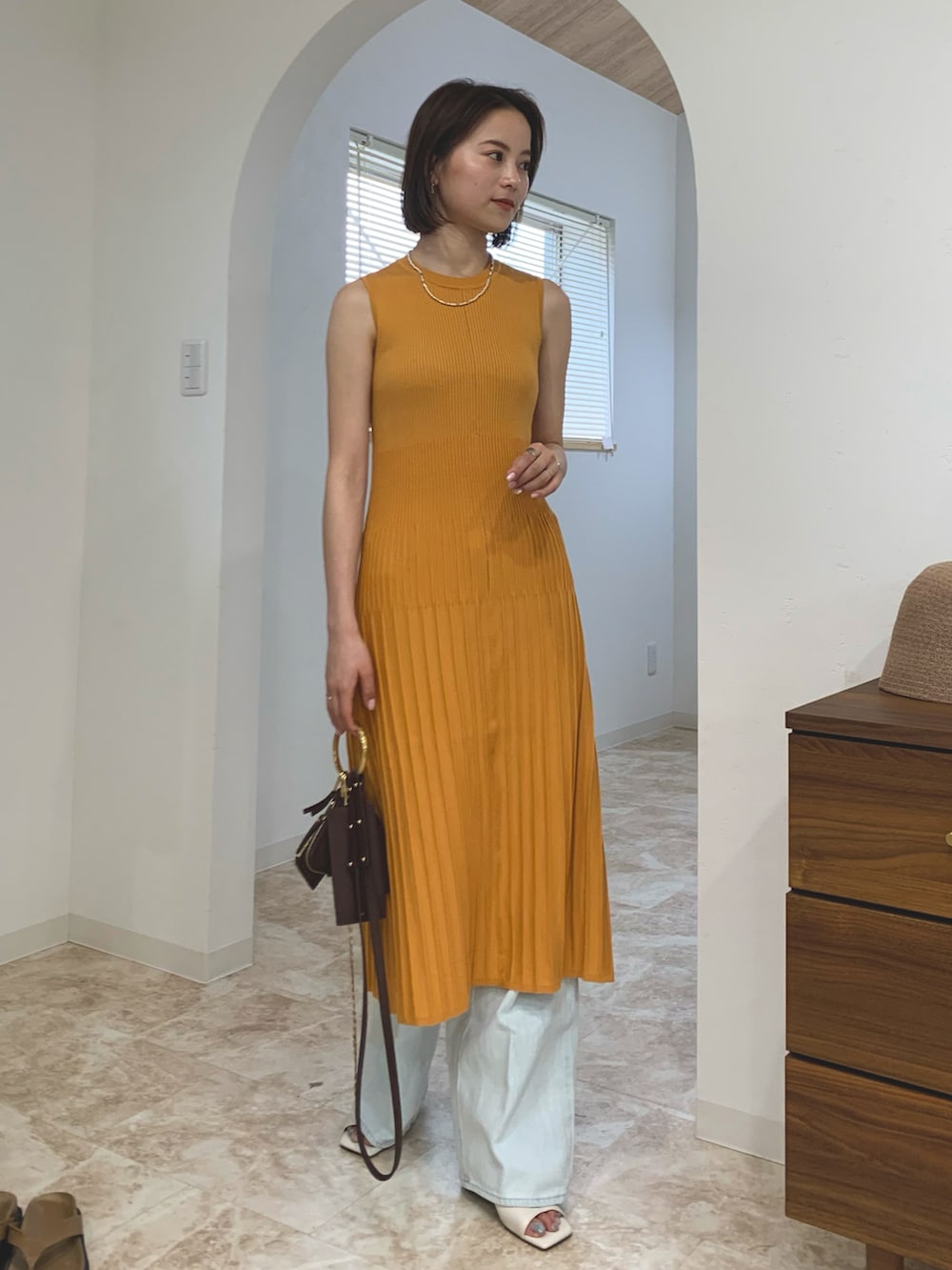 オレンジ系のワンピース、ブルー系のデニムパンツ、ブラウン系のバッグを着用したレディースの春コーディネートの2枚目の写真