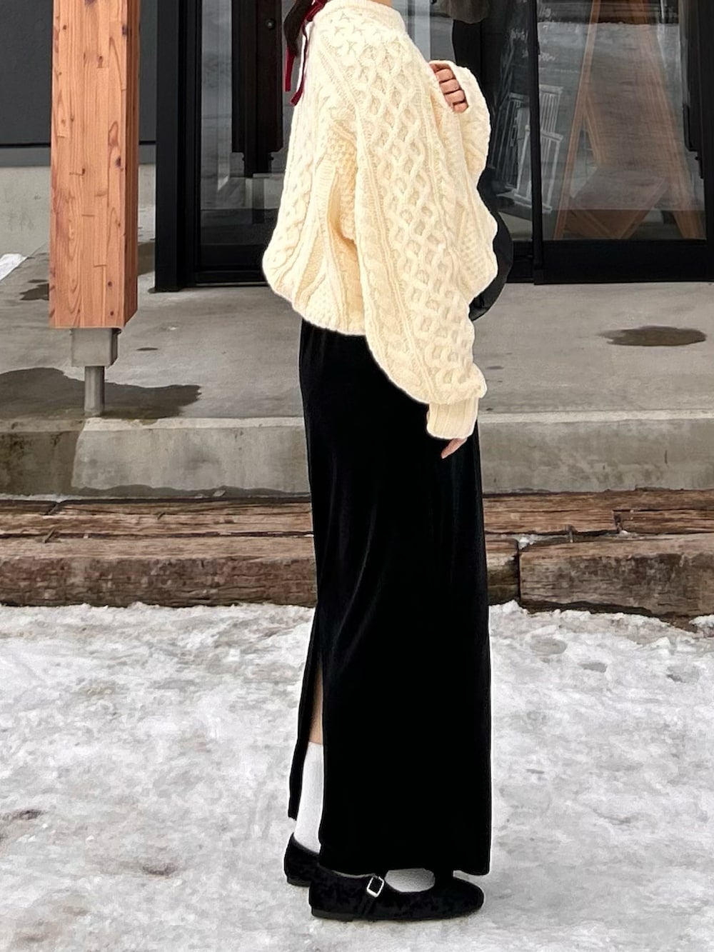 ブラック系のスカート、ホワイト系のニット/セーター、ブラック系のハンドバッグを着用したレディースの冬コーディネートの2枚目の写真