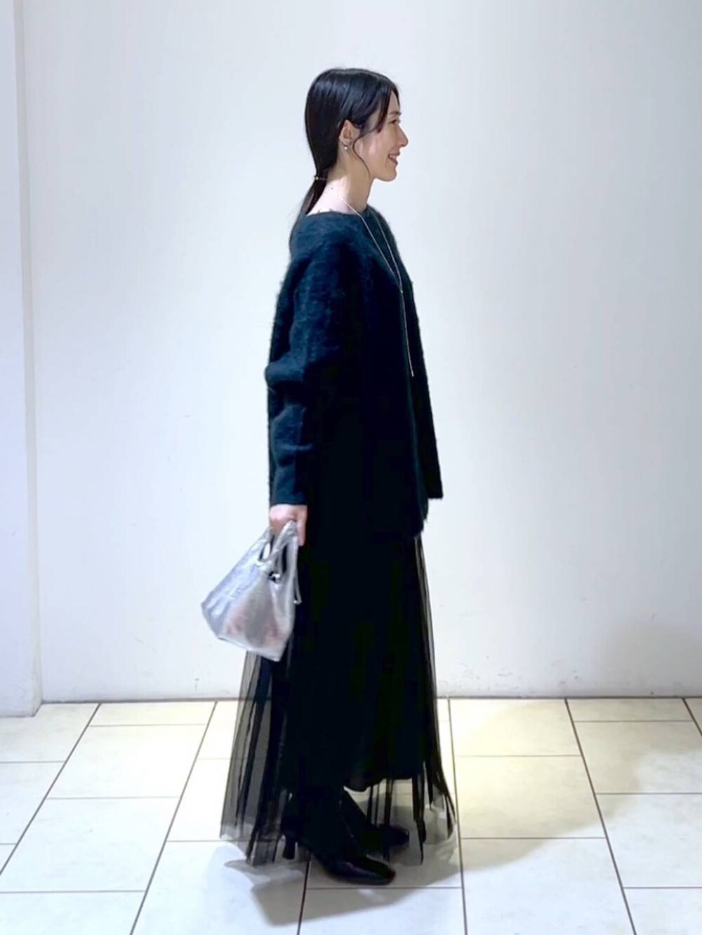 ブラック系のスカート、グリーン系のニット/セーター、シルバー系のショルダーバッグを着用したレディースの冬コーディネートの3枚目の写真