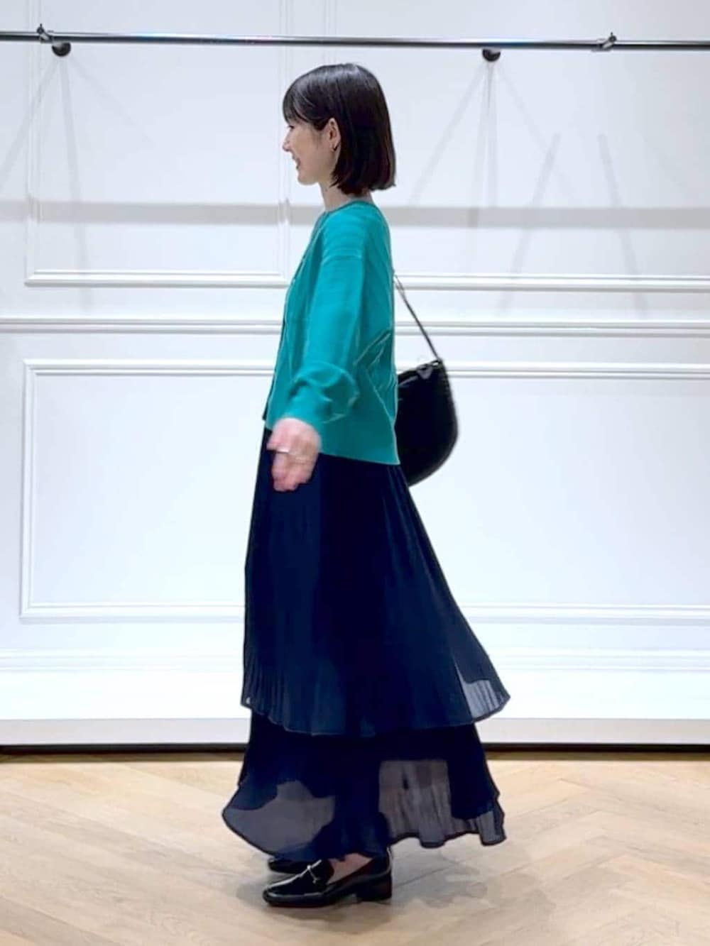 ブルー系のスカート、グリーン系のカーディガン/ボレロ、ブラック系のローファーを着用したレディースの春コーディネートの5枚目の写真