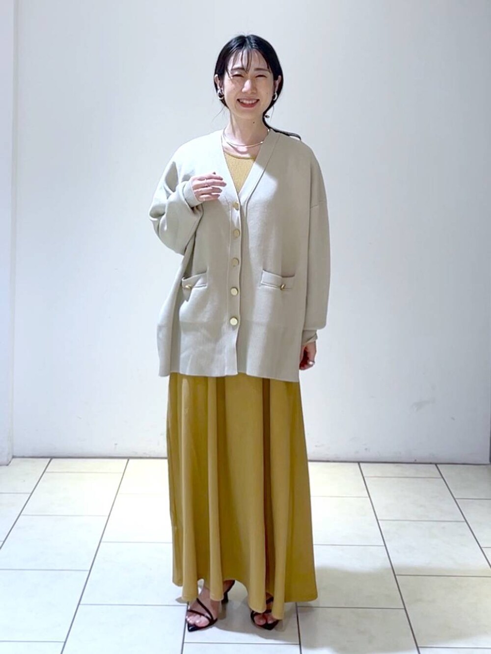 ブラック系のサンダル、オレンジ系のワンピース、ベージュ系のカーディガン/ボレロを着用したレディースの春コーディネートの6枚目の写真