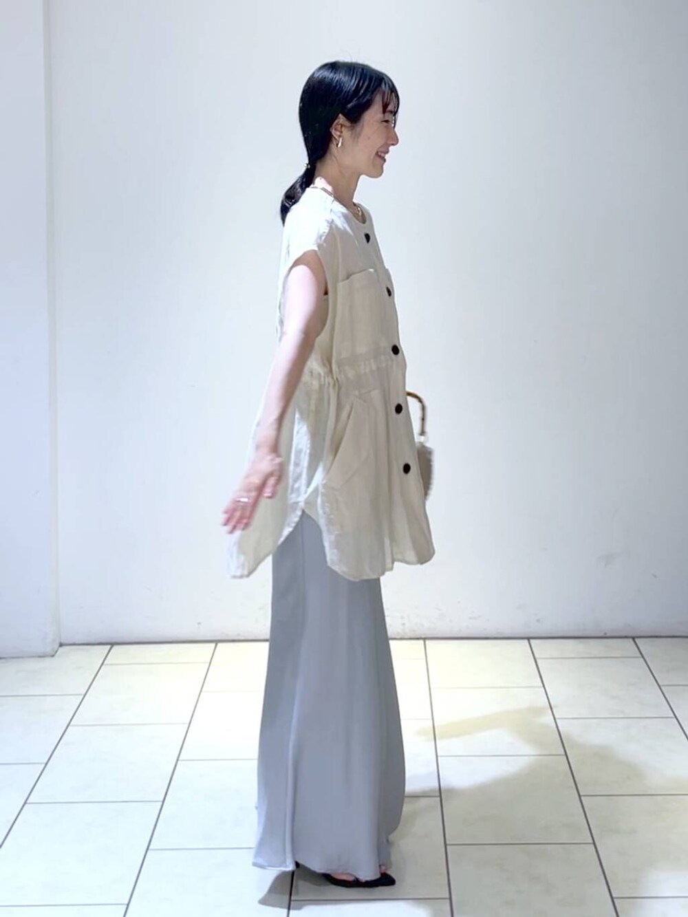 ベージュ系のショルダーバッグ、ベージュ系のベスト、ブルー系のスカートを着用したレディースの夏コーディネートの3枚目の写真