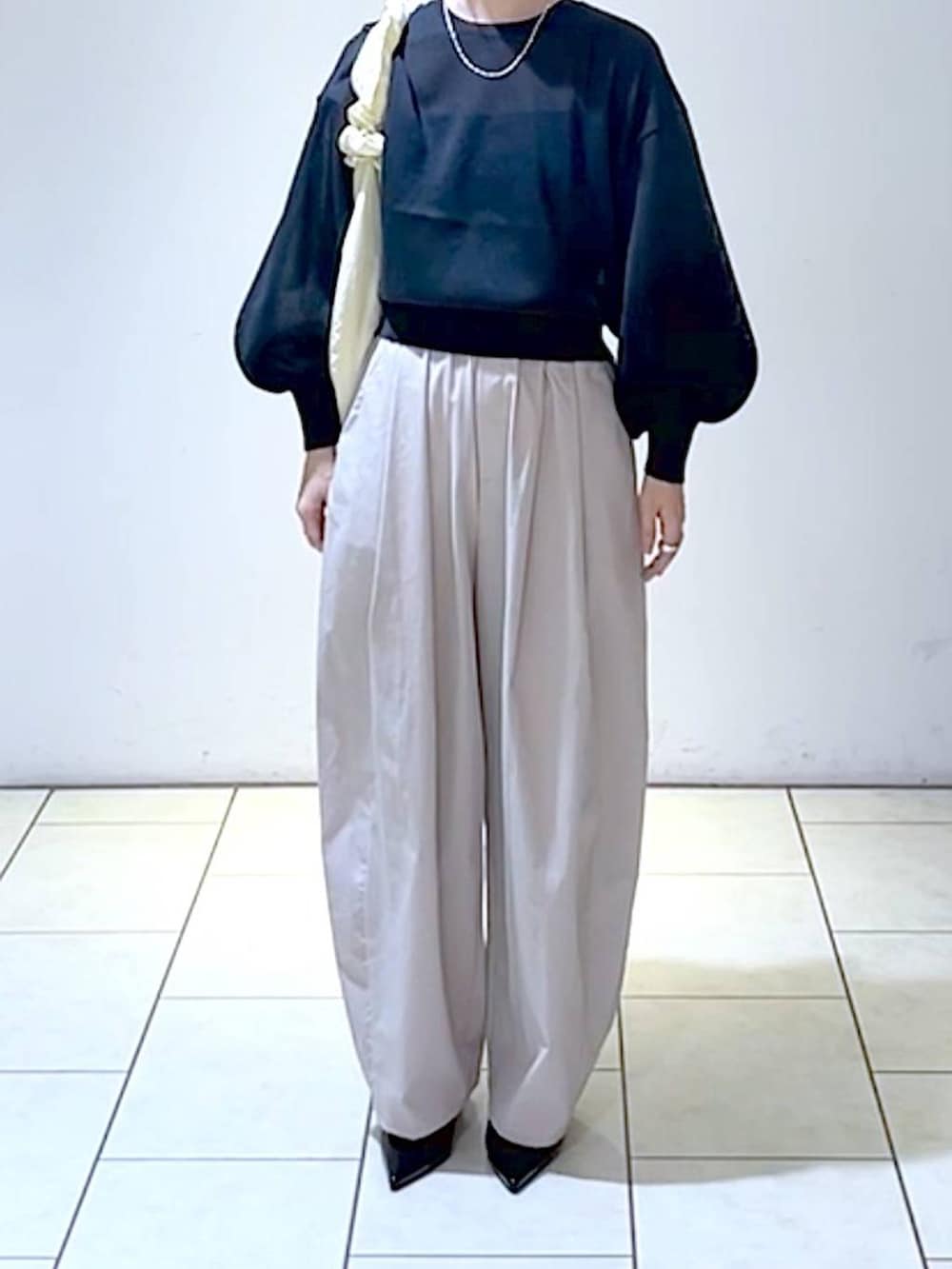 ブラック系のニット/セーター、ブラック系のパンプス、ホワイト系のショルダーバッグを着用したレディースの秋コーディネートの2枚目の写真