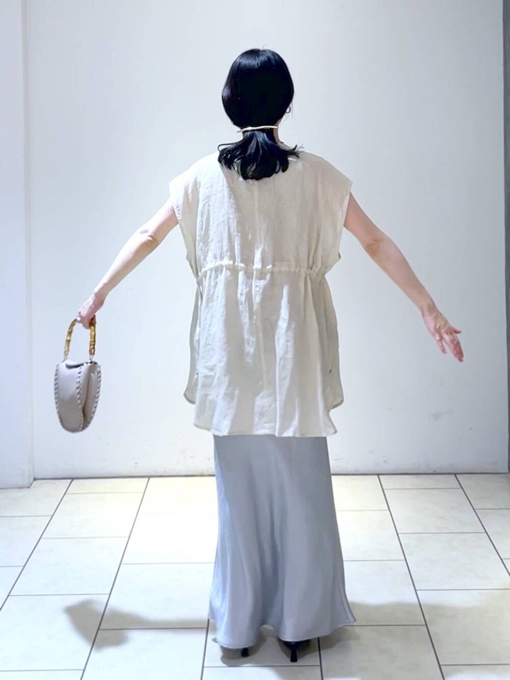 ベージュ系のショルダーバッグ、ベージュ系のベスト、ブルー系のスカートを着用したレディースの夏コーディネートの4枚目の写真