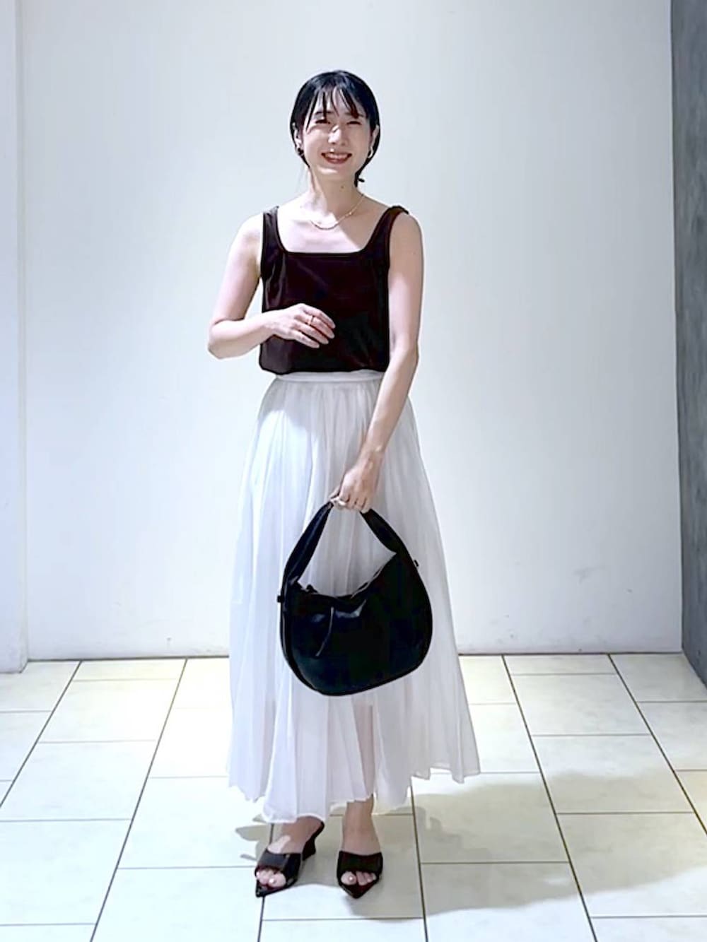 ブラック系のサンダル、ブラック系のハンドバッグ、ホワイト系のスカートを着用したレディースの夏コーディネートの6枚目の写真