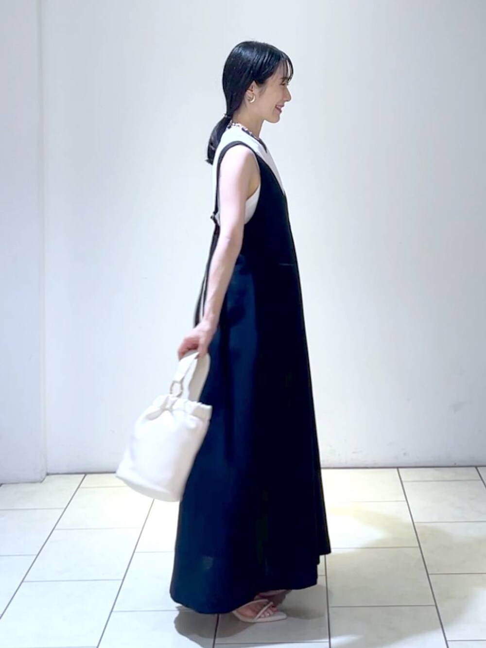 ホワイト系のサンダル、ブラック系のジャンパースカート、ホワイト系のショルダーバッグを着用したレディースの夏コーディネートの3枚目の写真