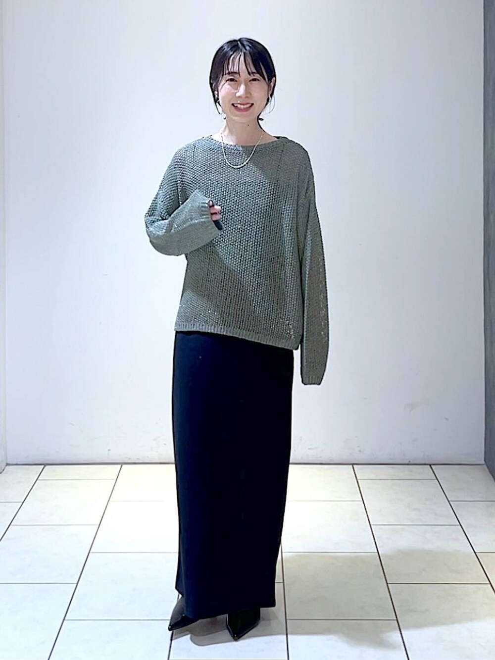 グリーン系のニット/セーター、ブラック系のパンプス、ブラック系のスカートを着用したレディースの秋コーディネートの6枚目の写真