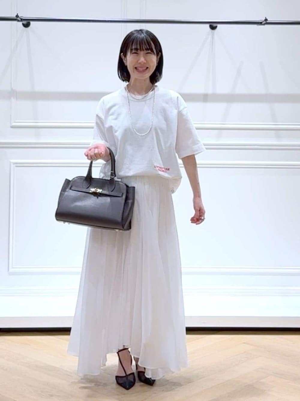 ホワイト系のスカート、ブラック系のパンプス、ブラウン系のショルダーバッグを着用したレディースの春コーディネートの6枚目の写真