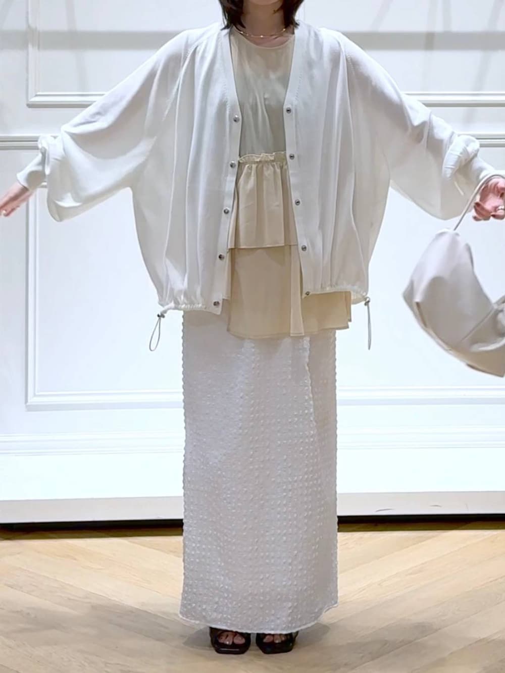 ホワイト系のカーディガン/ボレロ、ホワイト系のショルダーバッグ、ブラック系のパンプスを着用したレディースの夏コーディネートの2枚目の写真