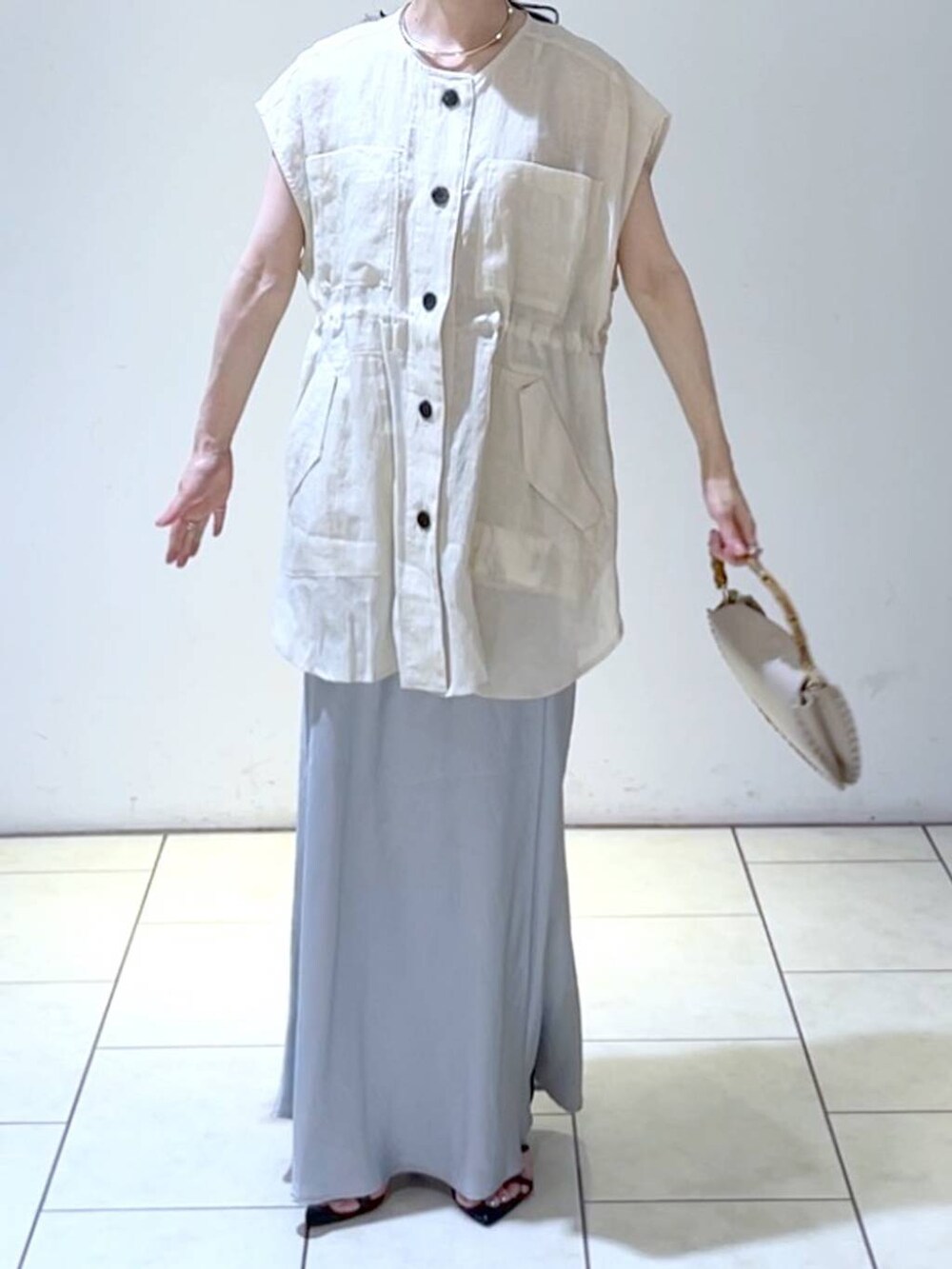 ベージュ系のショルダーバッグ、ベージュ系のベスト、ブルー系のスカートを着用したレディースの夏コーディネートの2枚目の写真