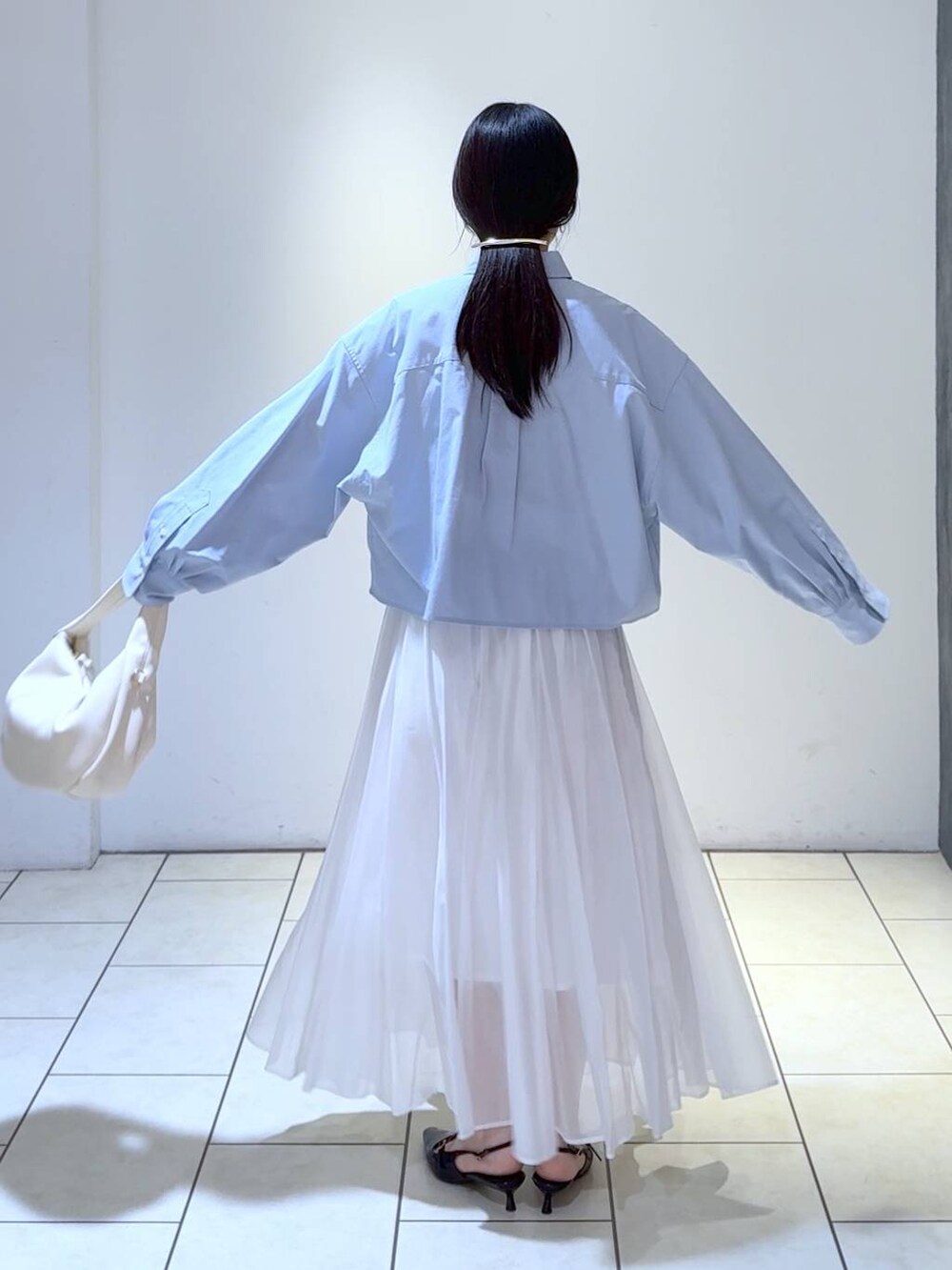 ホワイト系のハンドバッグ、ブルー系のシャツ/ブラウス、ブラック系のパンプスを着用したレディースの冬コーディネートの3枚目の写真