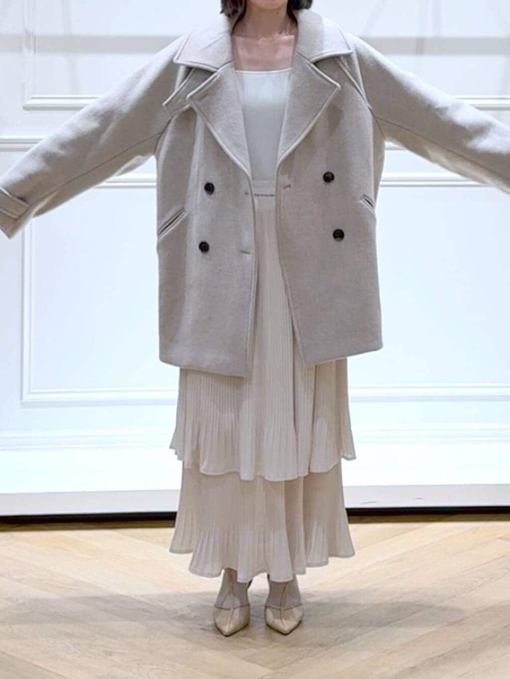 ベージュ系のピーコート、ホワイト系のスカート、ホワイト系のニット/セーターを着用したレディースの春コーディネートの2枚目の写真