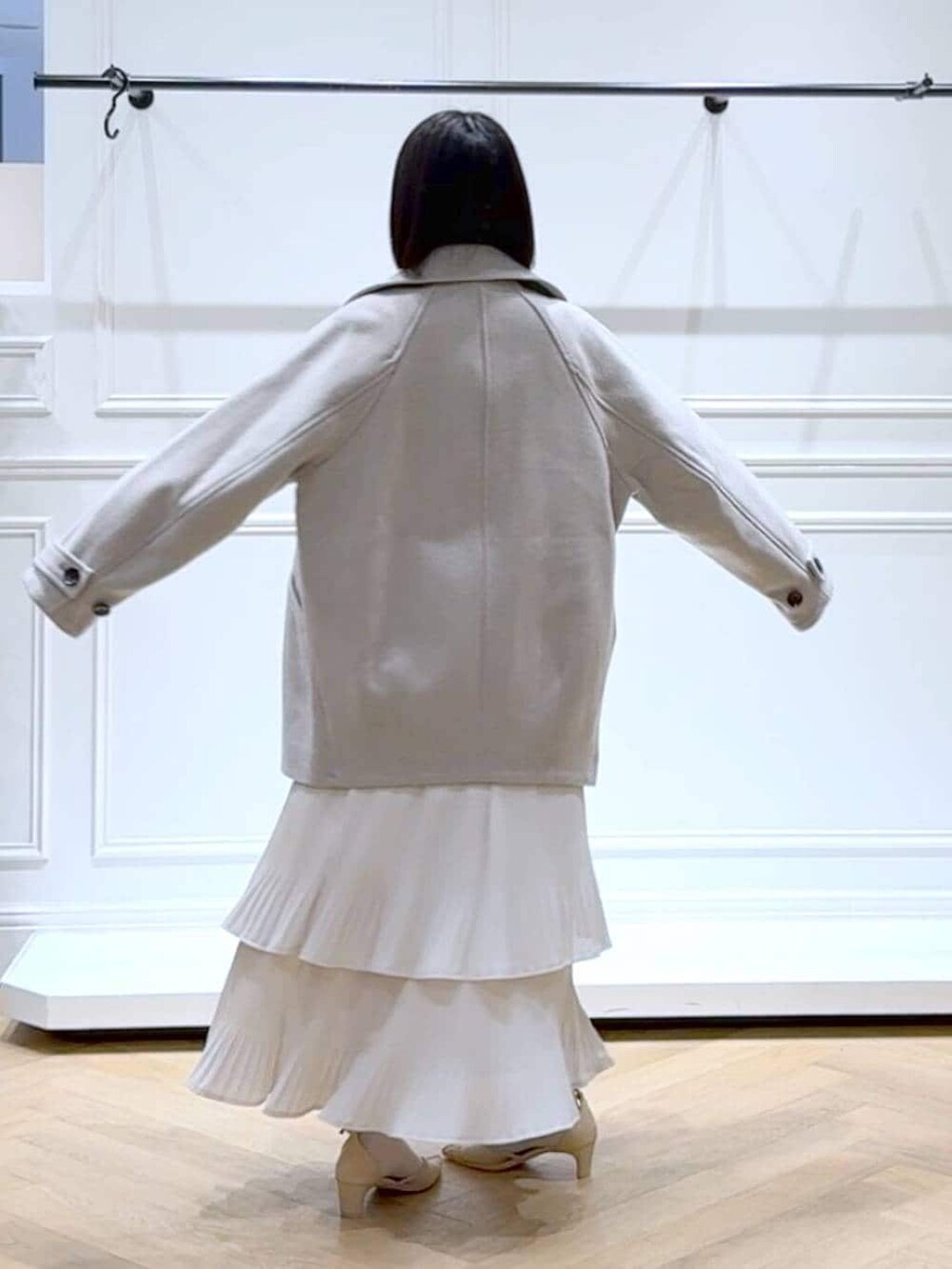 ベージュ系のピーコート、ホワイト系のスカート、ホワイト系のニット/セーターを着用したレディースの春コーディネートの4枚目の写真