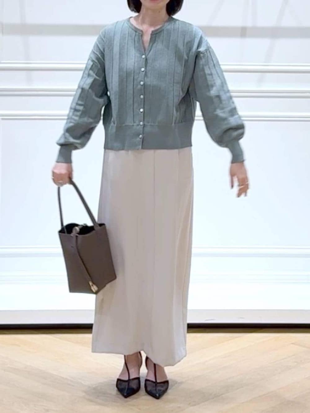 グリーン系のカーディガン/ボレロ、ブラック系のパンプス、ブラウン系のショルダーバッグを着用したレディースの春コーディネートの2枚目の写真