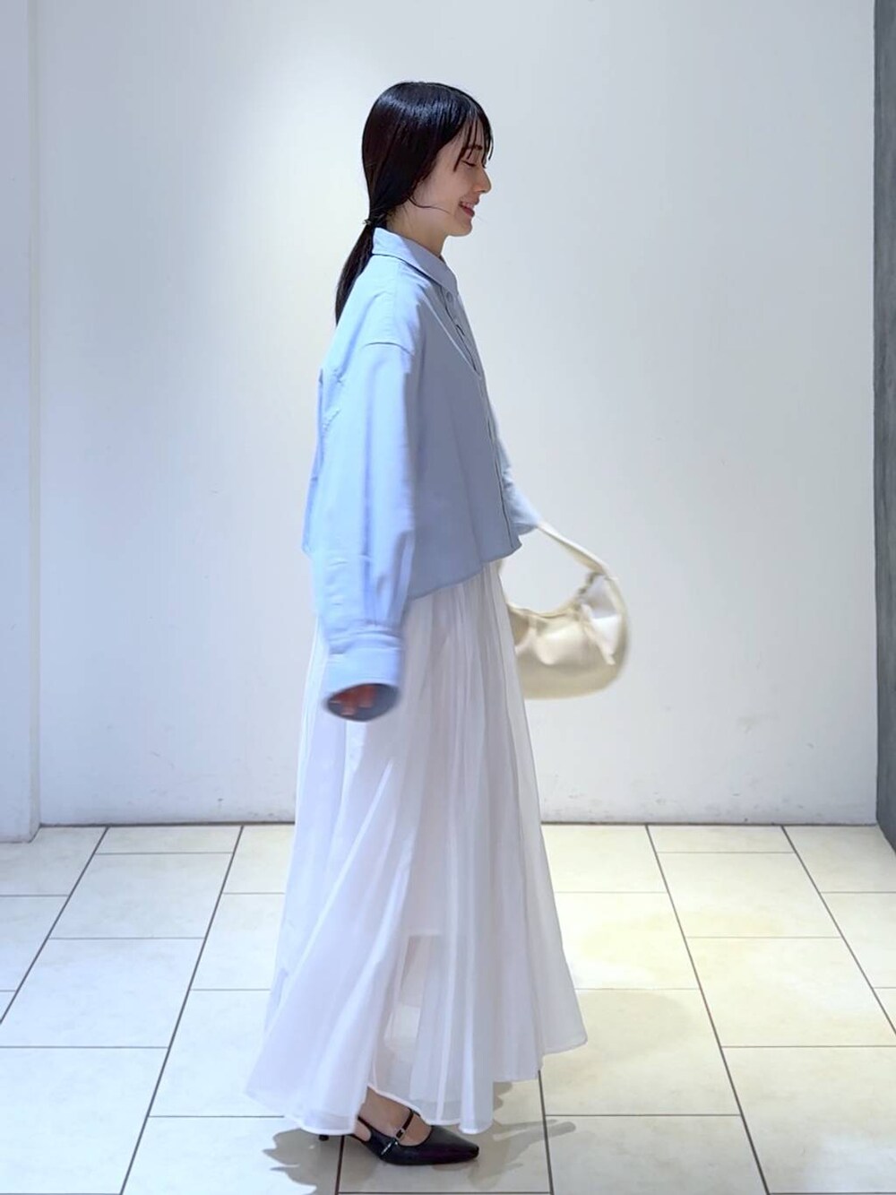 ホワイト系のハンドバッグ、ブルー系のシャツ/ブラウス、ブラック系のパンプスを着用したレディースの冬コーディネートの2枚目の写真