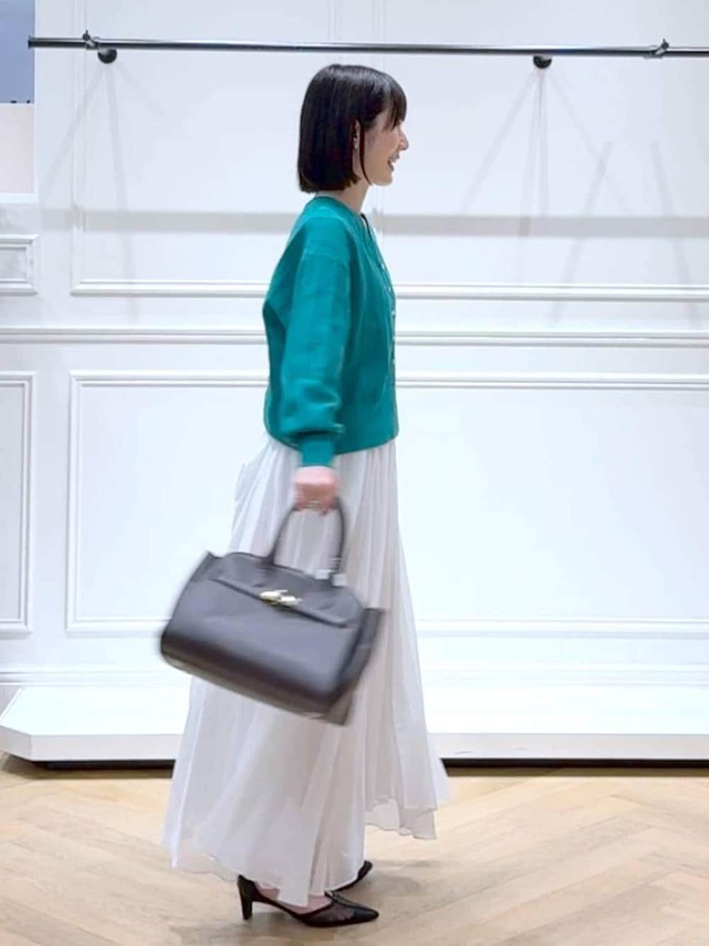 グリーン系のカーディガン/ボレロ、ホワイト系のスカート、ブラック系のパンプスを着用したレディースの春コーディネートの3枚目の写真