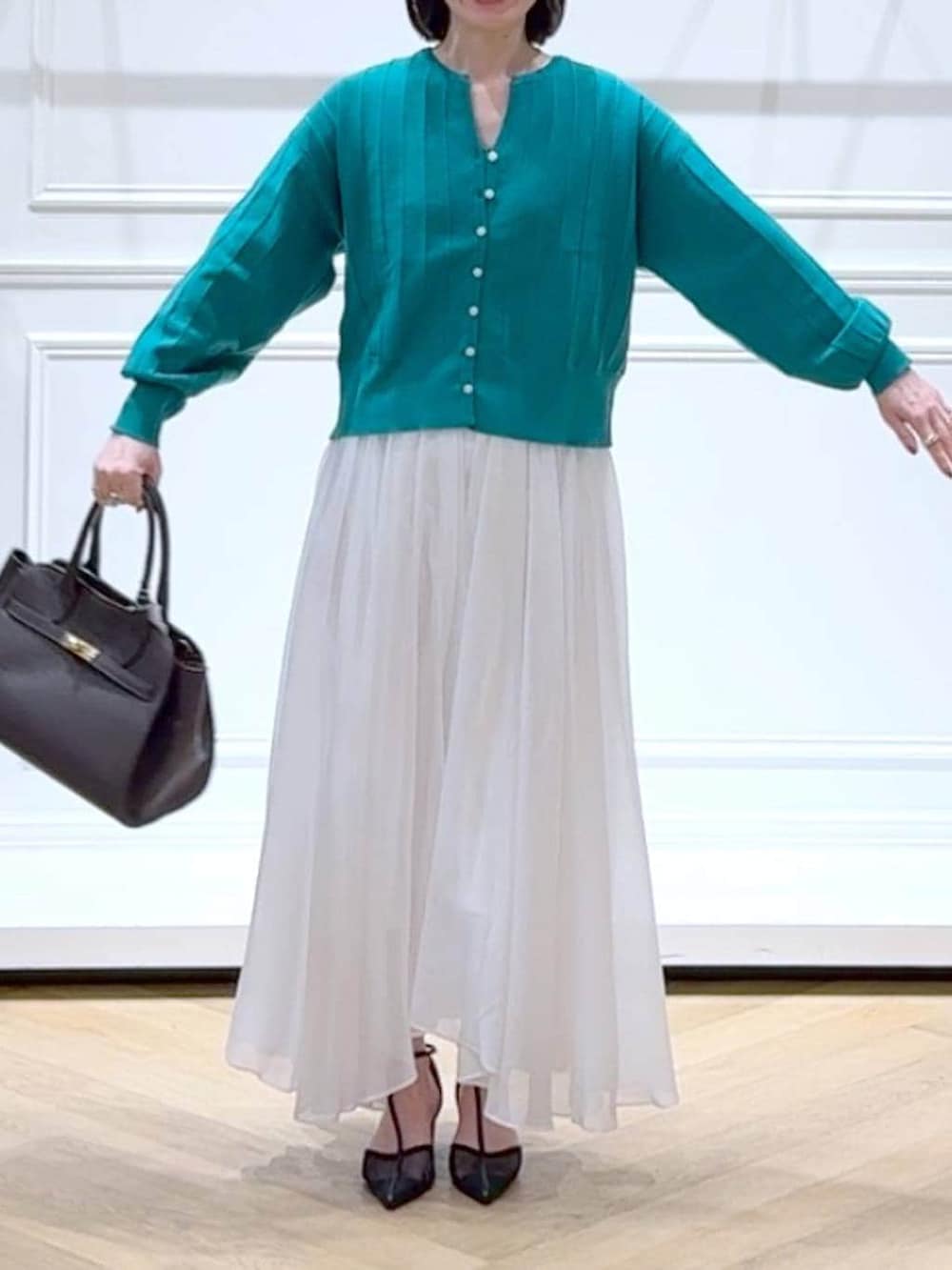 グリーン系のカーディガン/ボレロ、ホワイト系のスカート、ブラック系のパンプスを着用したレディースの春コーディネートの2枚目の写真