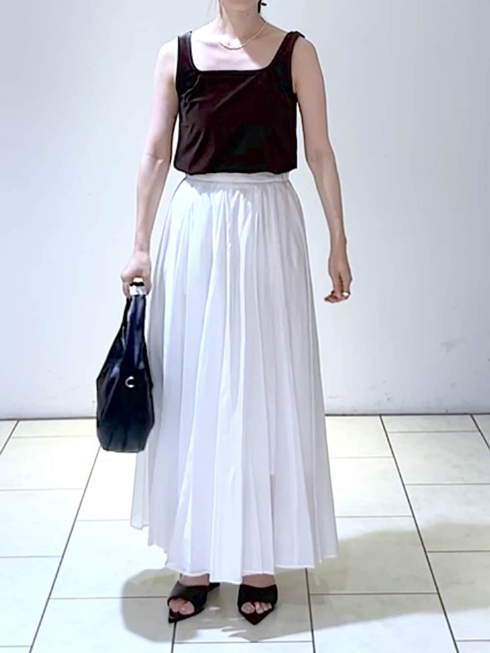 ブラック系のサンダル、ブラック系のハンドバッグ、ホワイト系のスカートを着用したレディースの夏コーディネートの2枚目の写真