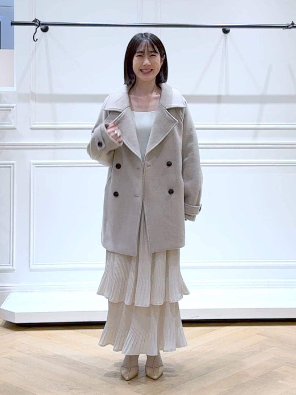 ベージュ系のピーコート、ホワイト系のスカート、ホワイト系のニット/セーターを着用したレディースの春コーディネートの6枚目の写真