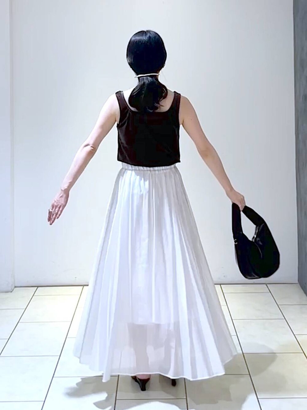 ブラック系のサンダル、ブラック系のハンドバッグ、ホワイト系のスカートを着用したレディースの夏コーディネートの4枚目の写真