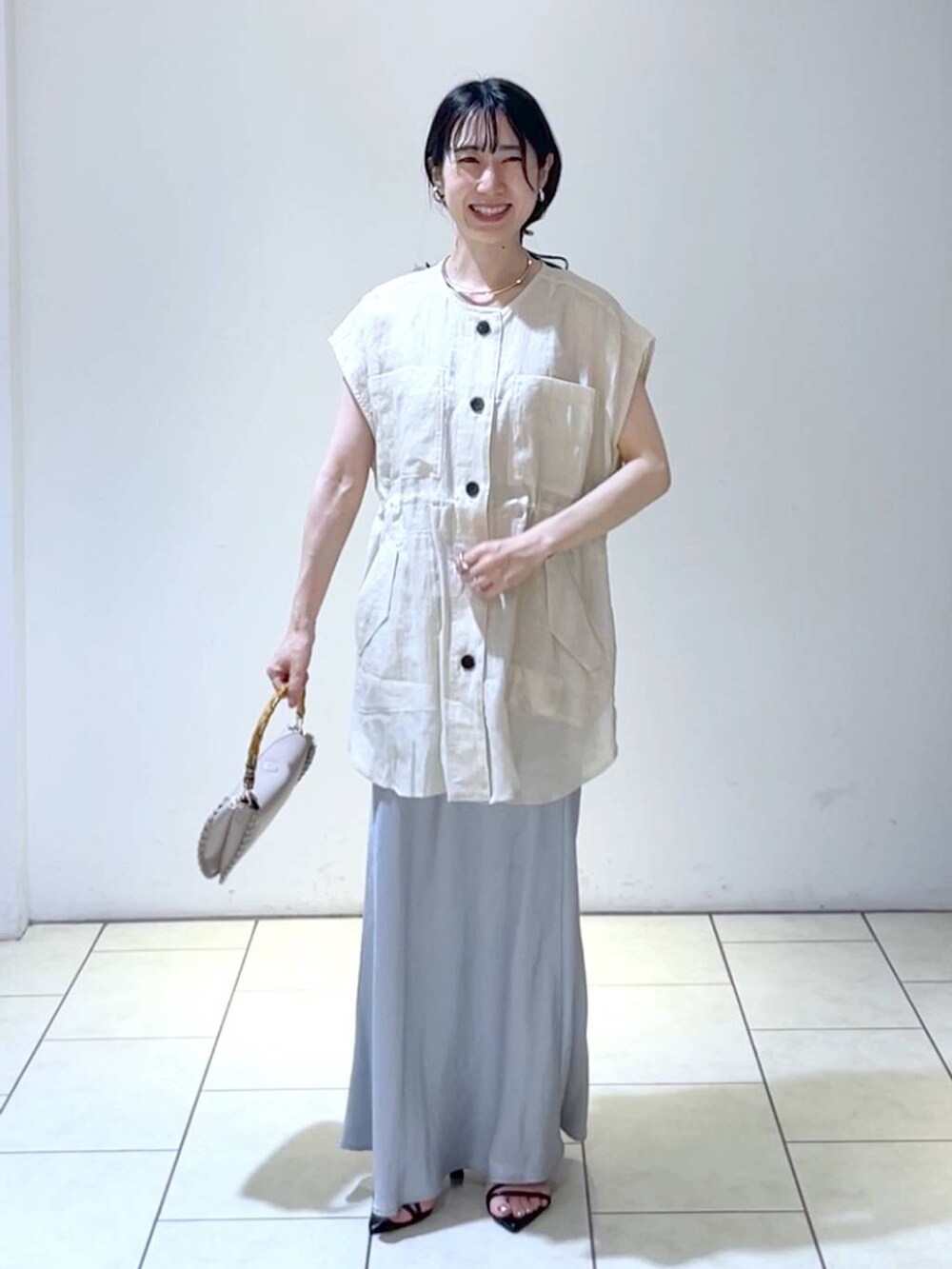 ベージュ系のショルダーバッグ、ベージュ系のベスト、ブルー系のスカートを着用したレディースの夏コーディネートの6枚目の写真