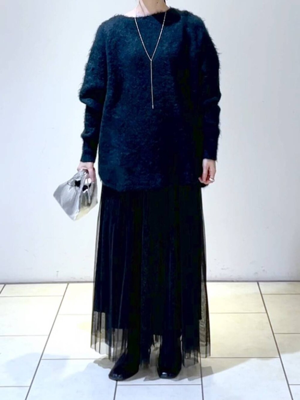 ブラック系のスカート、グリーン系のニット/セーター、シルバー系のショルダーバッグを着用したレディースの冬コーディネートの2枚目の写真