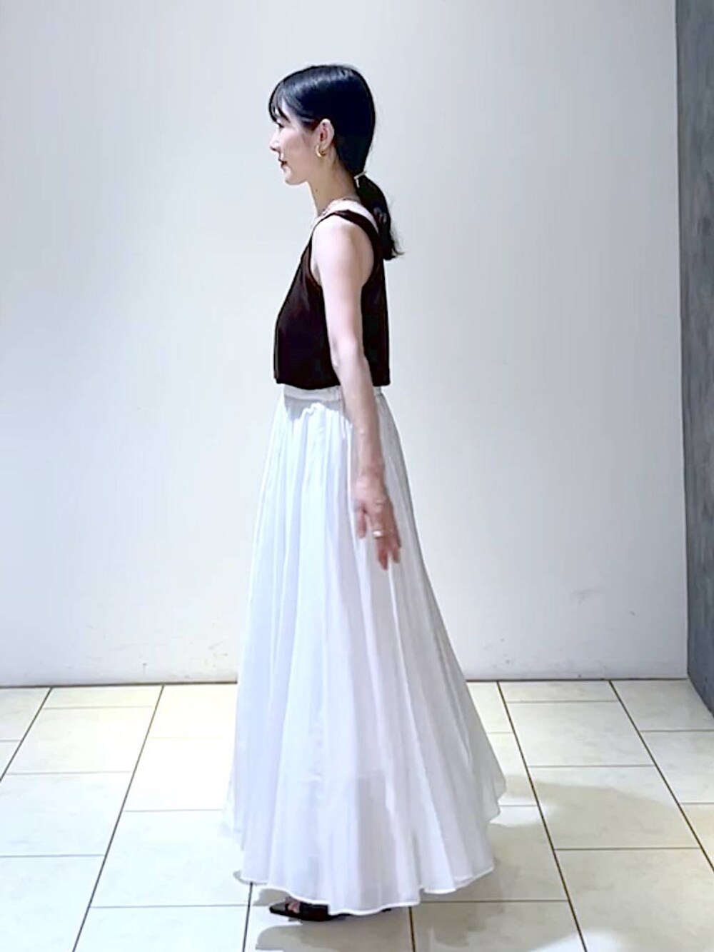 ブラック系のサンダル、ブラック系のハンドバッグ、ホワイト系のスカートを着用したレディースの夏コーディネートの5枚目の写真