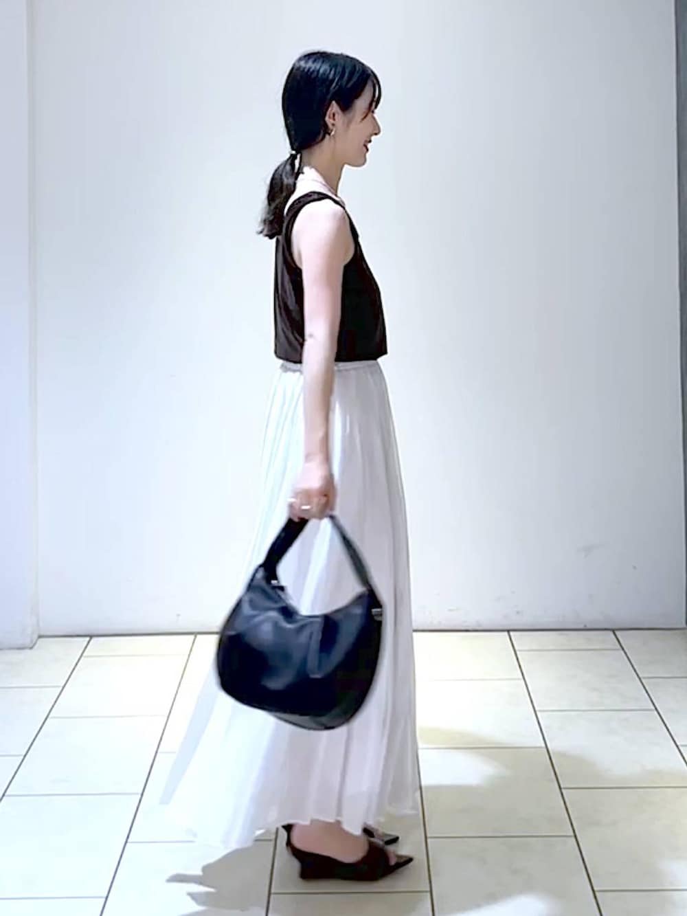ブラック系のサンダル、ブラック系のハンドバッグ、ホワイト系のスカートを着用したレディースの夏コーディネートの3枚目の写真