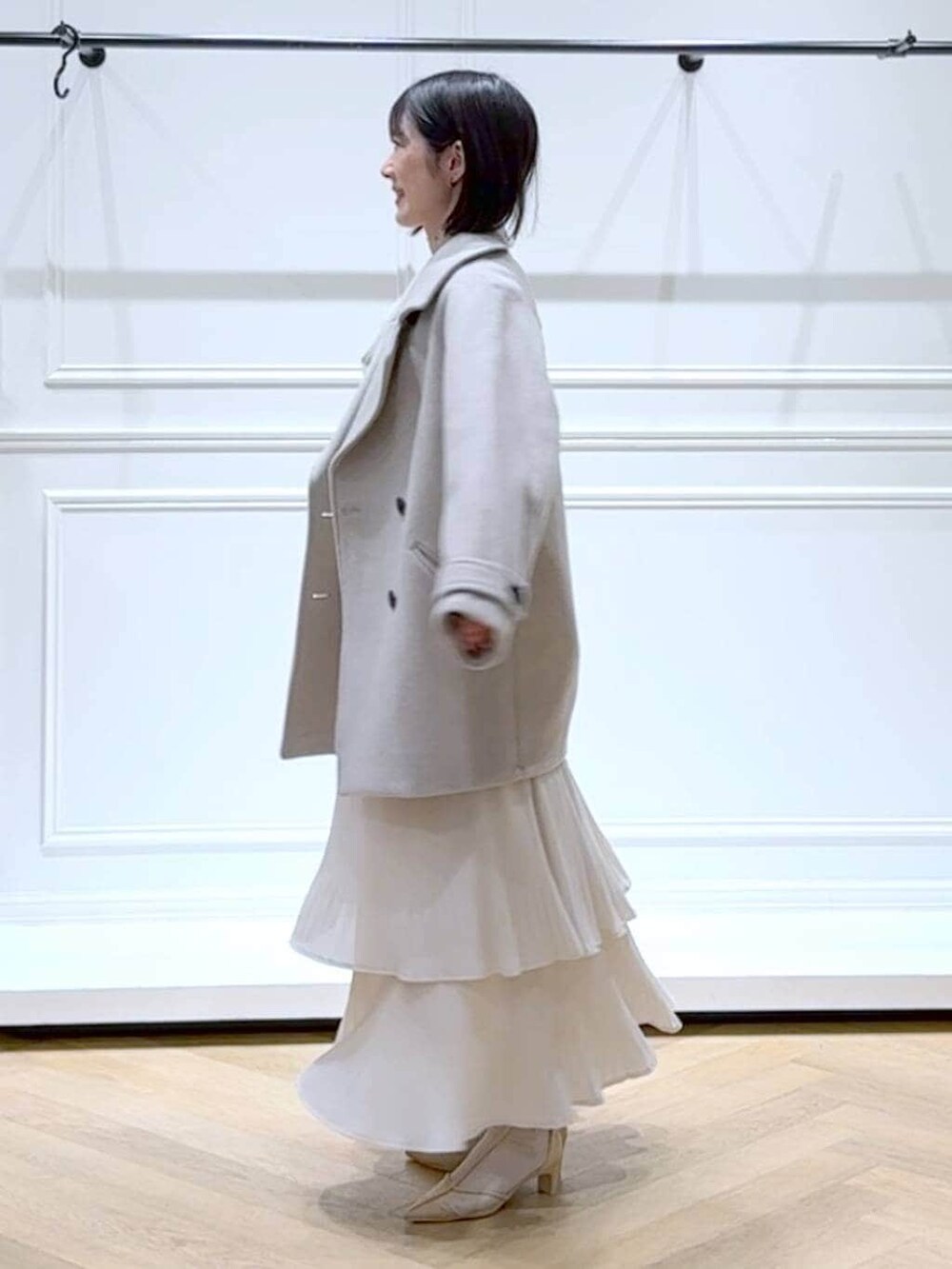 ベージュ系のピーコート、ホワイト系のスカート、ホワイト系のニット/セーターを着用したレディースの春コーディネートの5枚目の写真