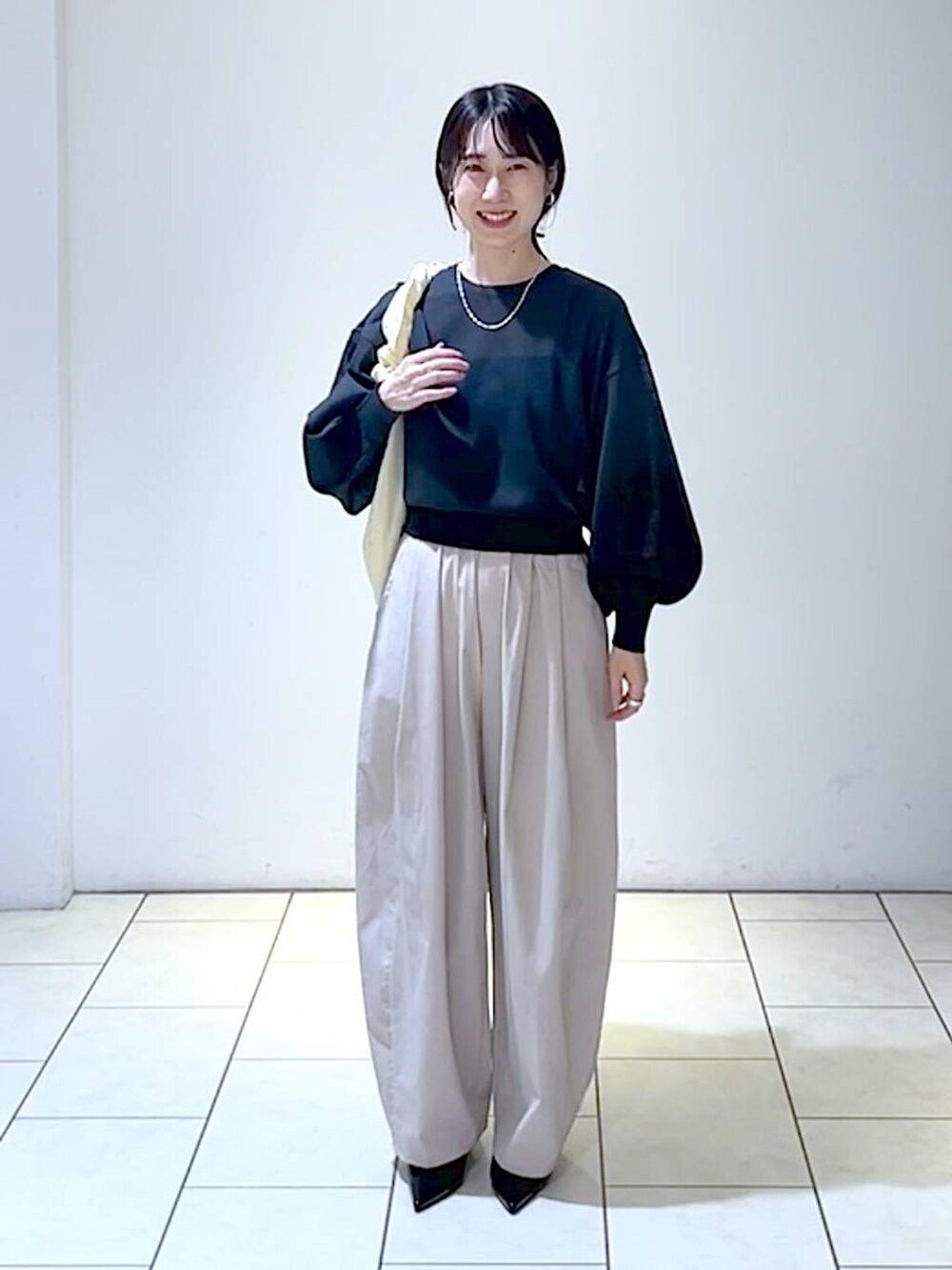 ブラック系のニット/セーター、ブラック系のパンプス、ホワイト系のショルダーバッグを着用したレディースの秋コーディネートの6枚目の写真