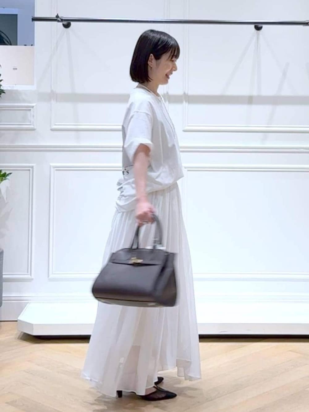 ホワイト系のスカート、ブラック系のパンプス、ブラウン系のショルダーバッグを着用したレディースの春コーディネートの3枚目の写真