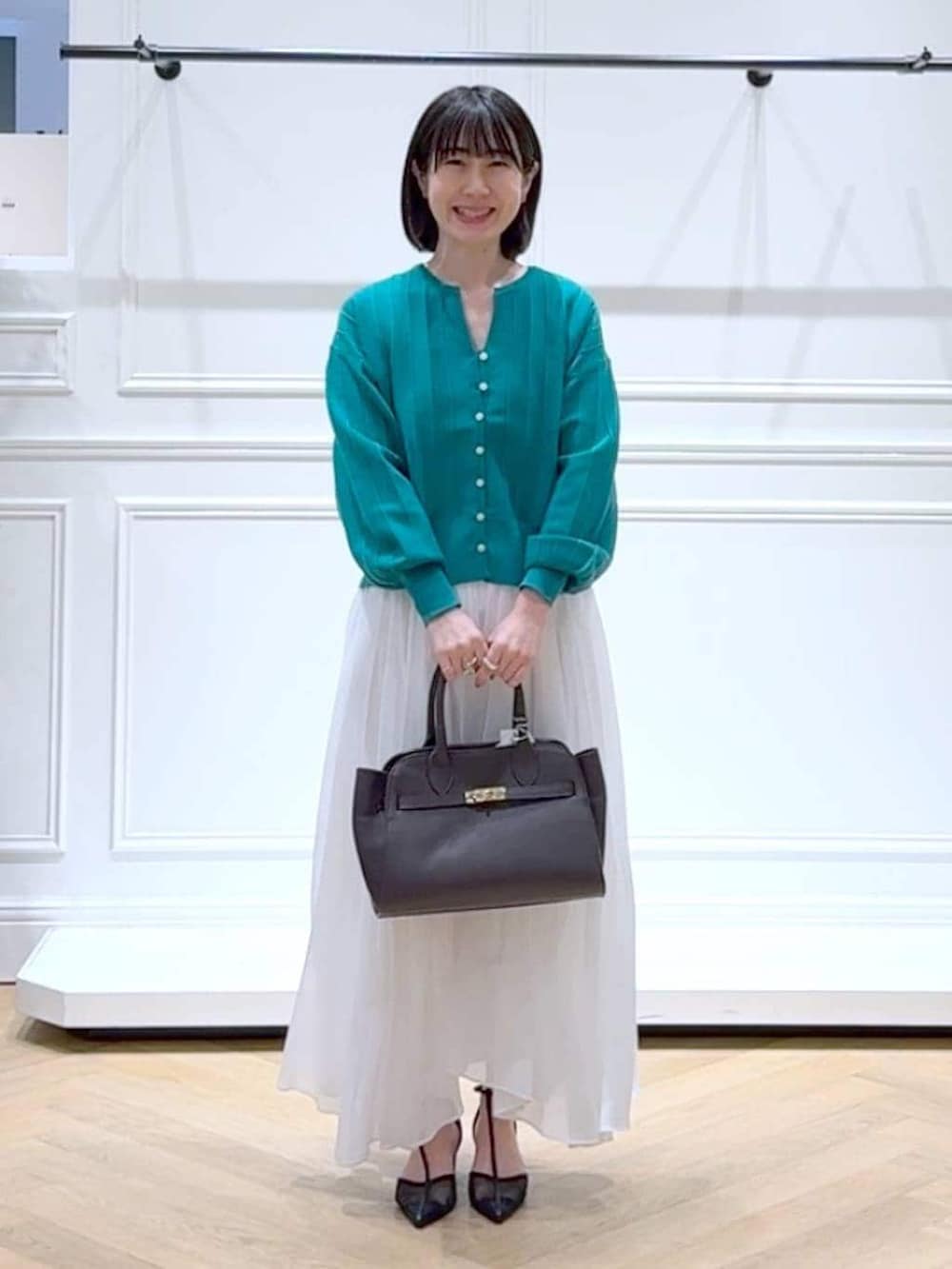 グリーン系のカーディガン/ボレロ、ホワイト系のスカート、ブラック系のパンプスを着用したレディースの春コーディネートの6枚目の写真