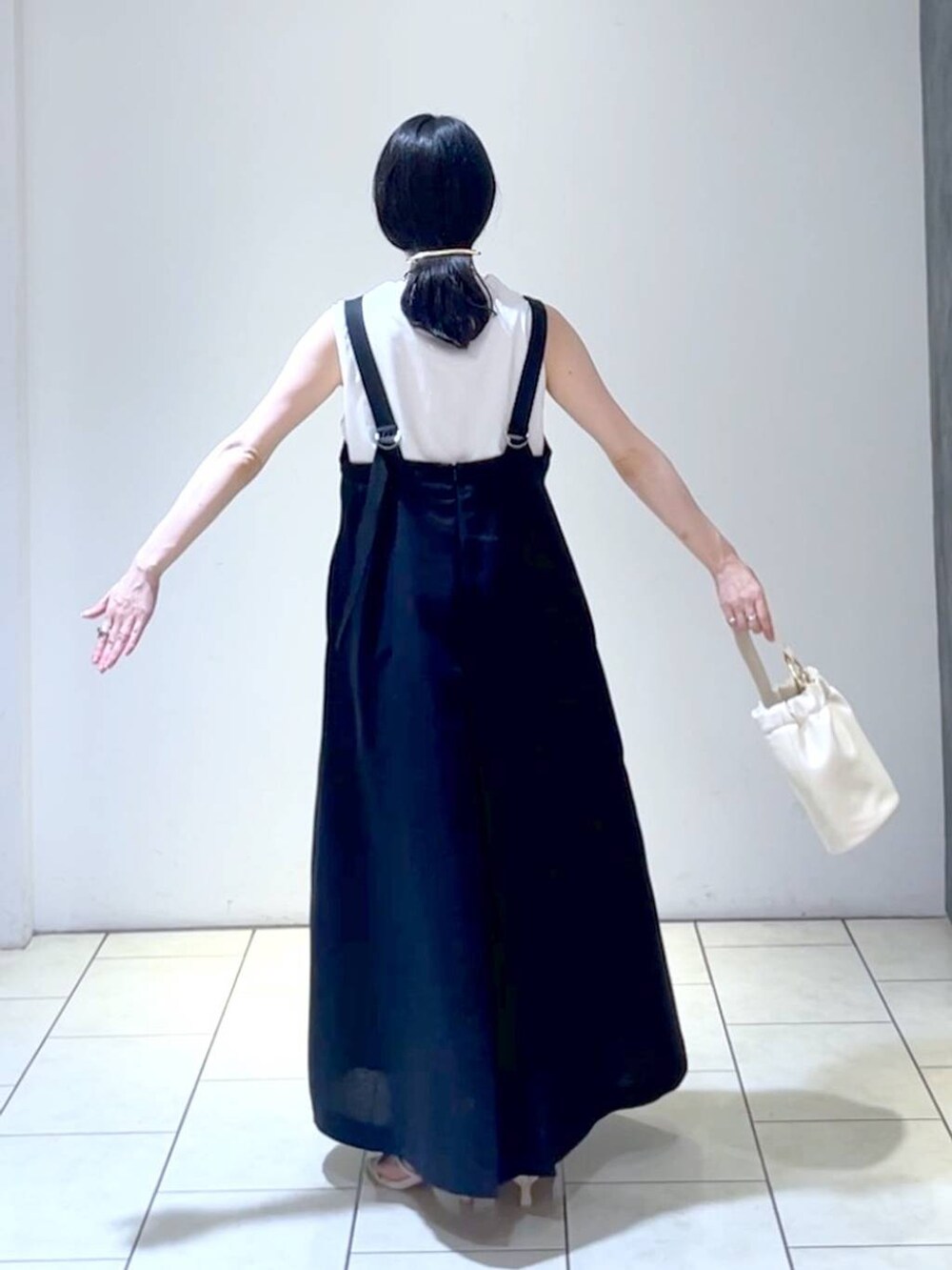 ホワイト系のサンダル、ブラック系のジャンパースカート、ホワイト系のショルダーバッグを着用したレディースの夏コーディネートの4枚目の写真