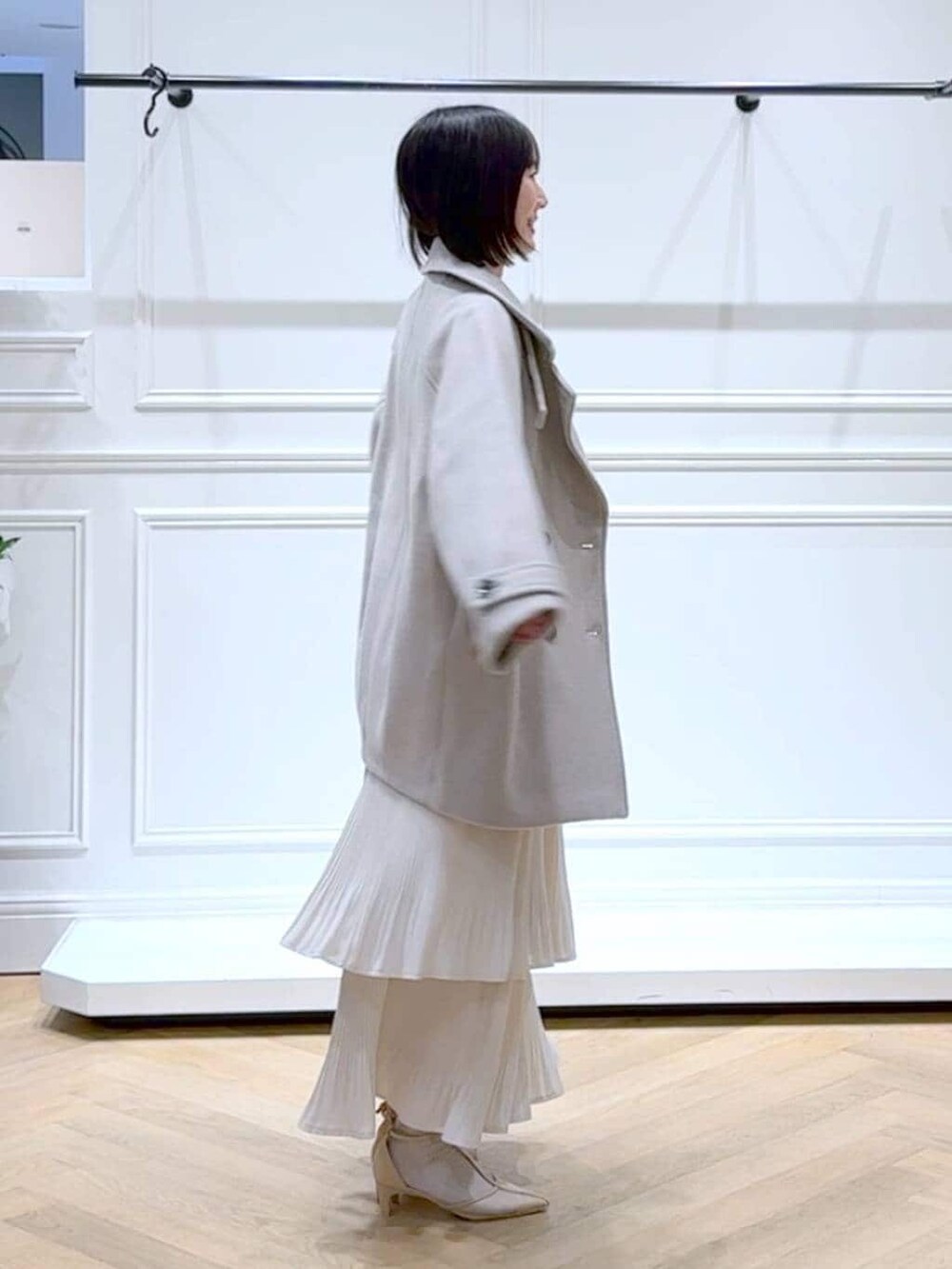 ベージュ系のピーコート、ホワイト系のスカート、ホワイト系のニット/セーターを着用したレディースの春コーディネートの3枚目の写真