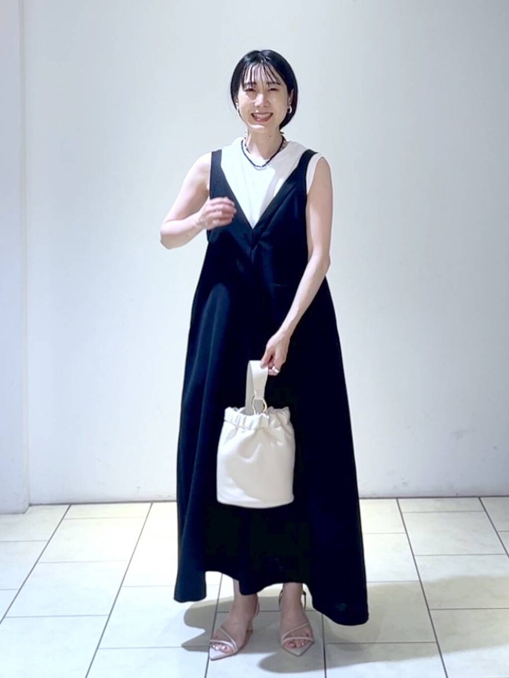 ホワイト系のサンダル、ブラック系のジャンパースカート、ホワイト系のショルダーバッグを着用したレディースの夏コーディネートの6枚目の写真