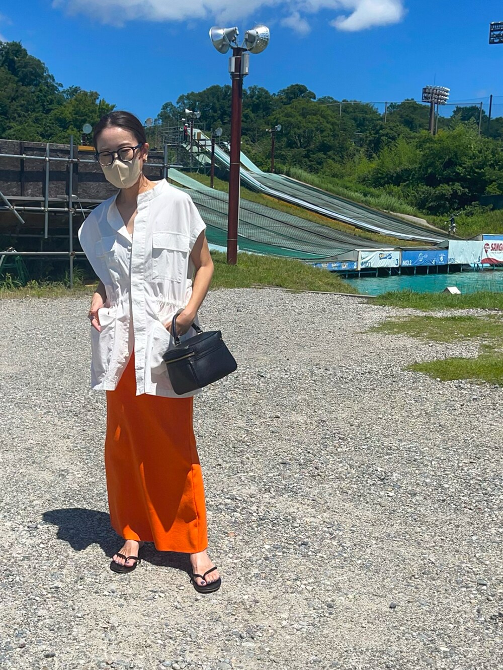 ブラック系のバッグ、オレンジ系のスカート、ブラック系のサンダルを着用したレディースの夏コーディネートの2枚目の写真