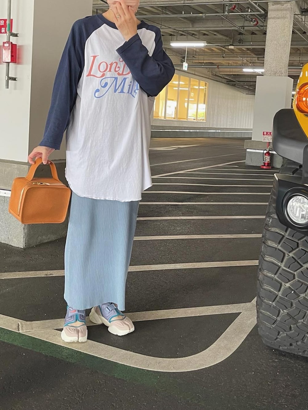 オレンジ系のハンドバッグ、ブルー系のスカート、その他のスニーカーを着用したレディースの夏コーディネートの2枚目の写真