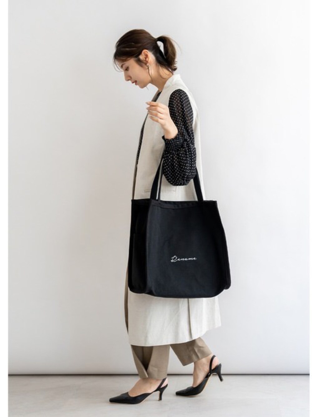 ベージュ系のトートバッグ、ブルー系のベスト、グレー系のスニーカーを着用したレディースの夏コーディネートの4枚目の写真