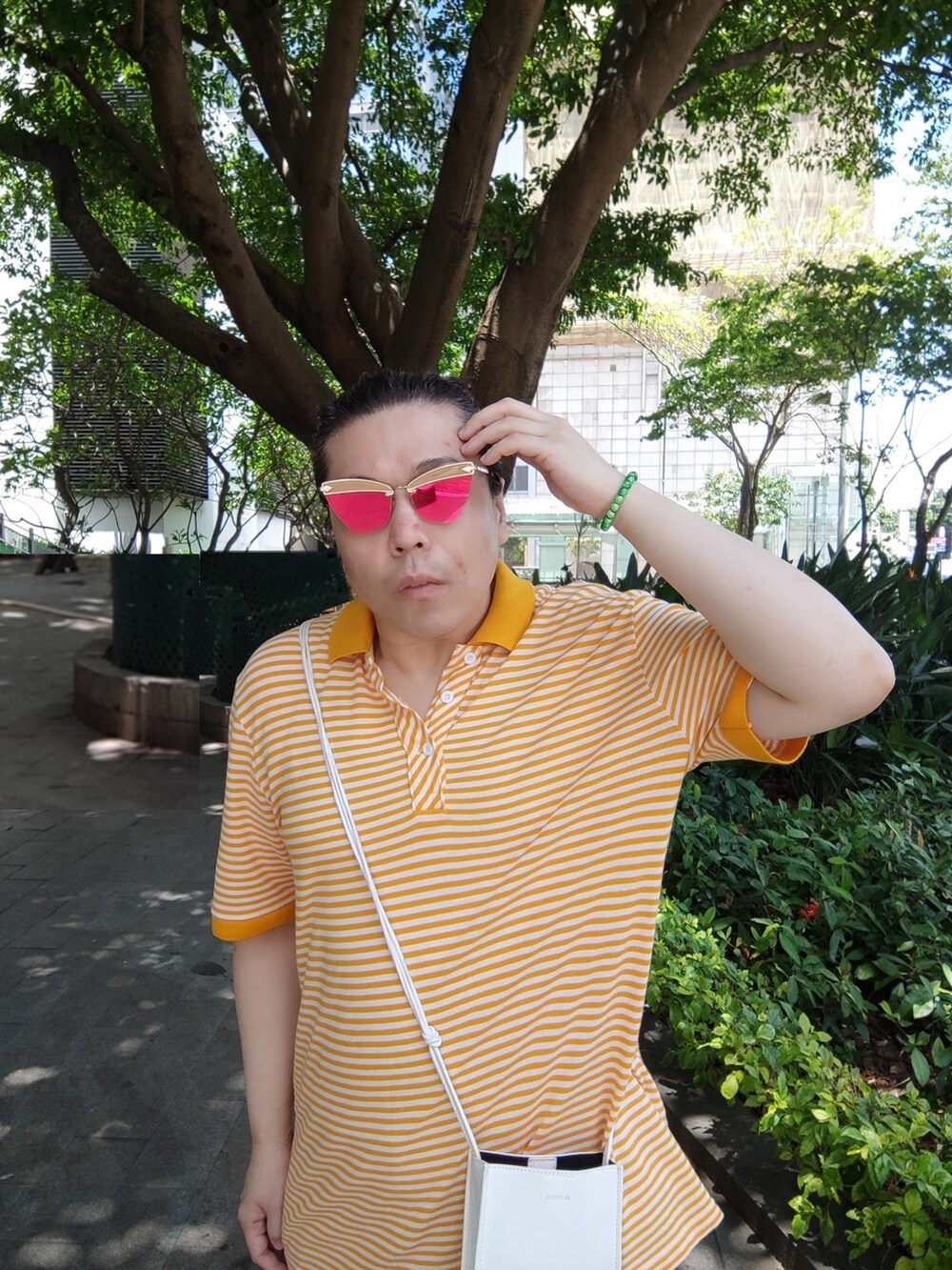 ホワイト系のバッグ、オレンジ系のポロシャツ、ベージュ系のチノパンツを着用したメンズの夏コーディネートの3枚目の写真